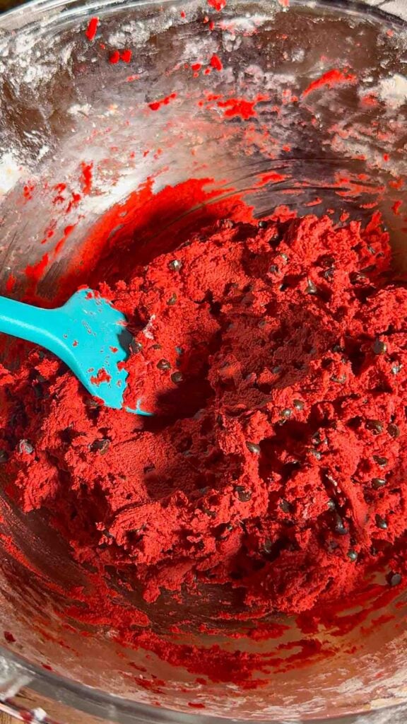 red velvet cookie dough in a mixing bowl loaded with chocolate chips