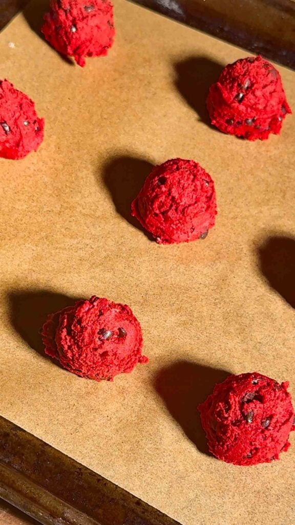 red velvet shortbread cookie dough balls on a parchment lined baking sheet
