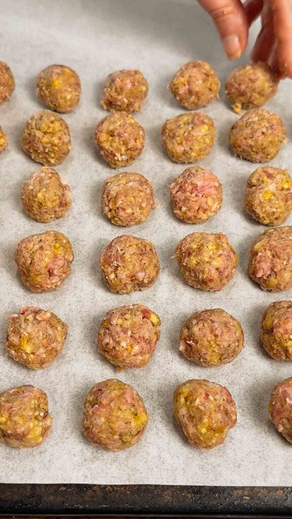 raw mini meatballs on a parchment lined baking sheet