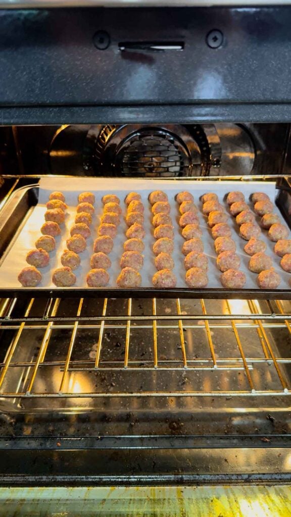 raw mini meatballs on a parchment lined baking sheet in the oven