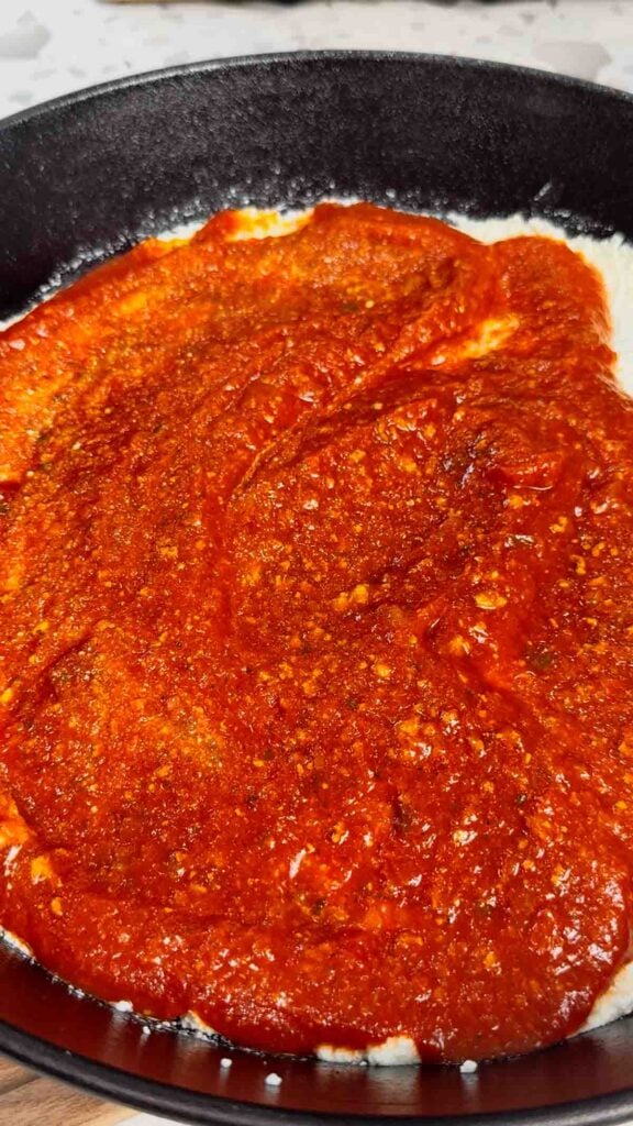 pasta sauce spread over ricotta in a cast iron skillet