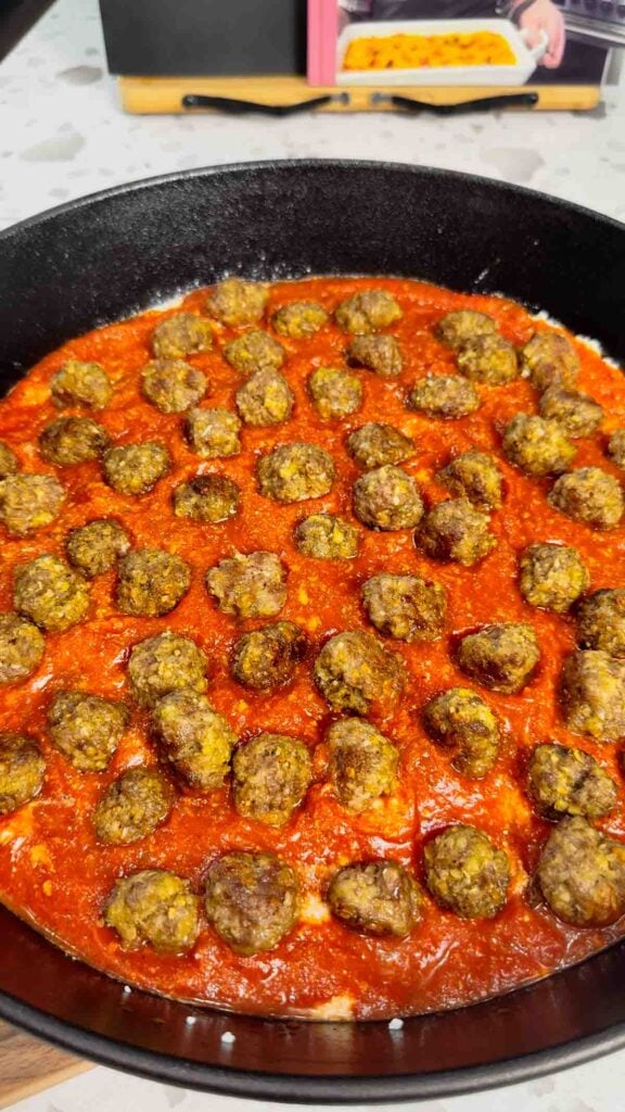 cooked mini meatballs on top of pasta sauce in a cast iron skillet