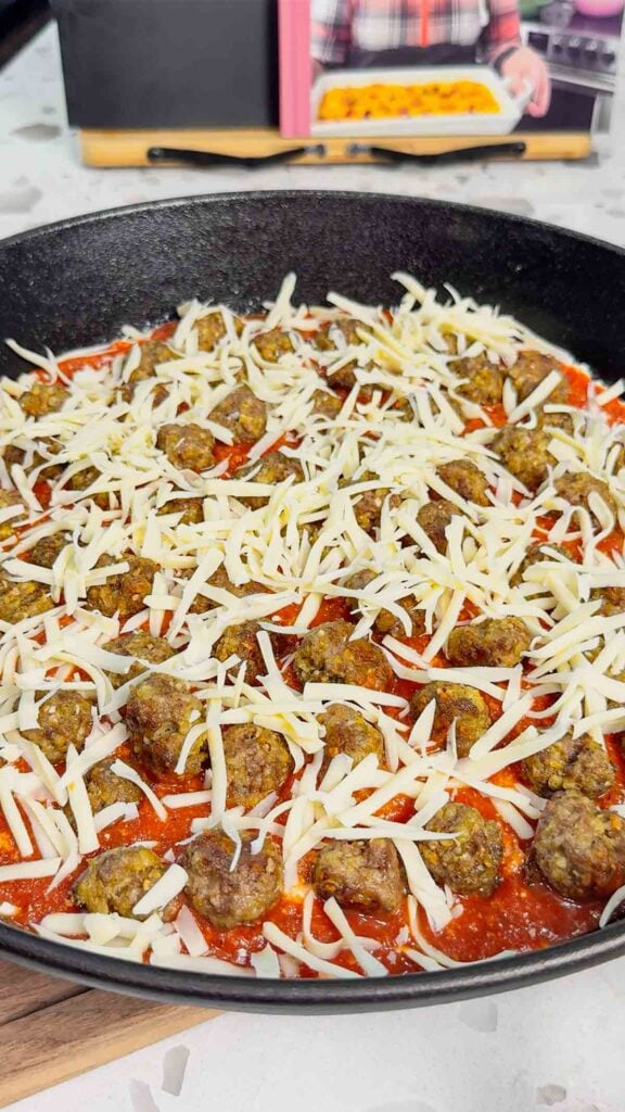 shredded cheese on top of mini meatballs and pasta sauce