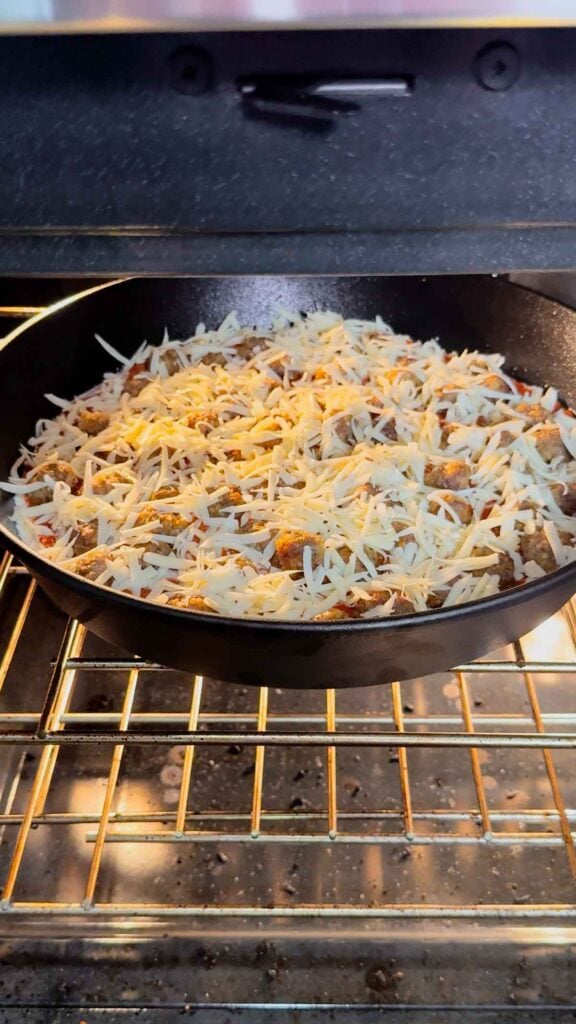 meatball dip covered in shredded cheese in a cast iron skillet in the oven