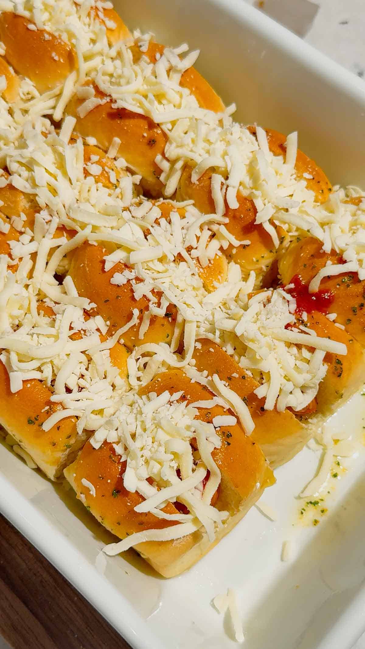 shredded mozzarella cheese on top of mini hot dogs in a baking dish