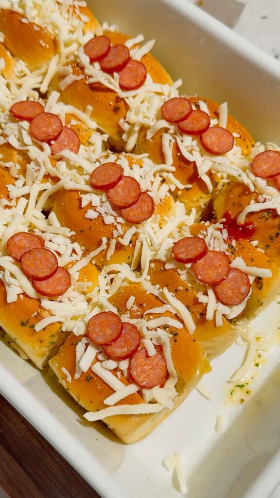 mini pepperoni slices on top of mini hot dogs in a baking dish