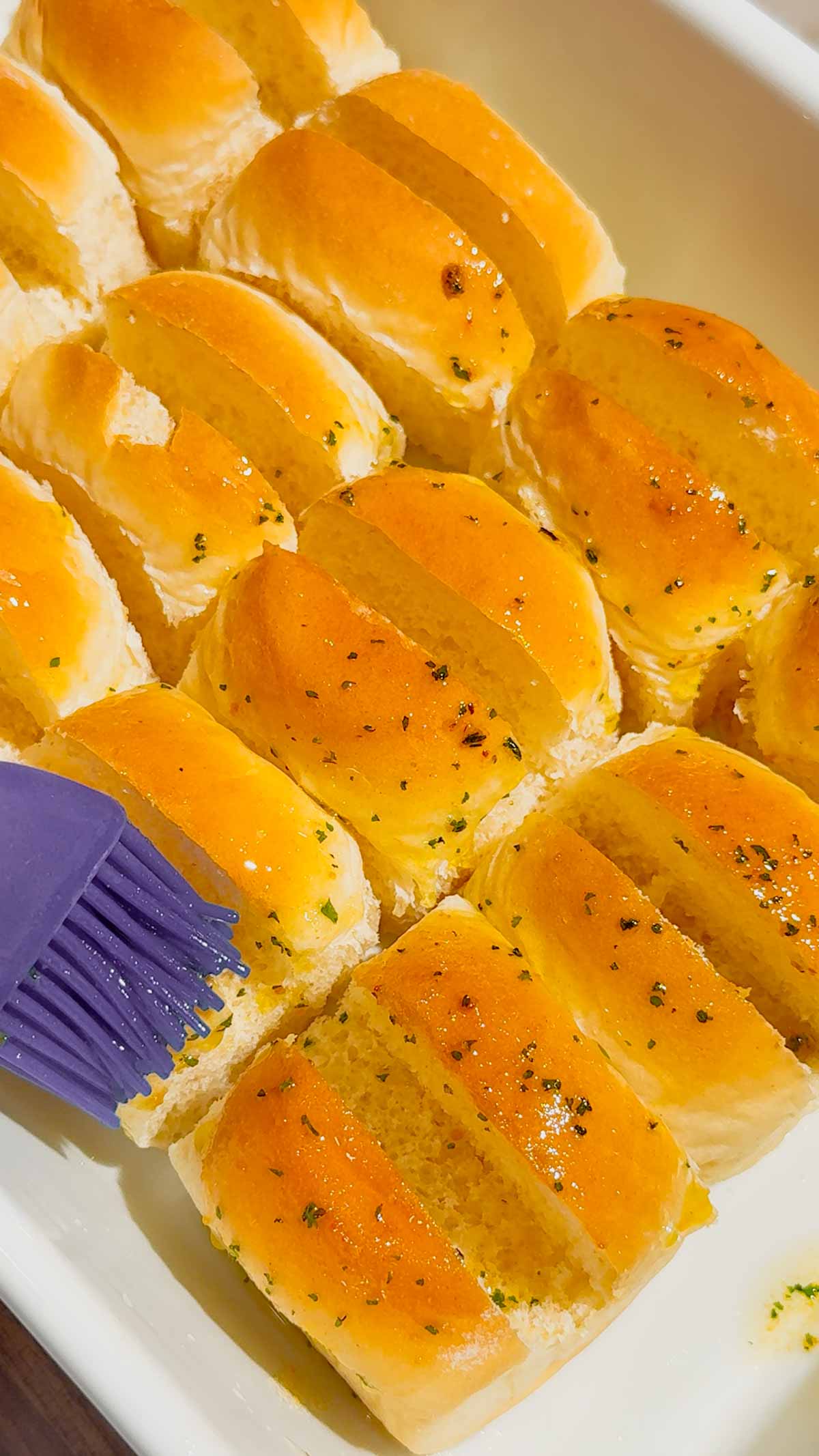brushing garlic butter on Hawaiian rolls in a baking dish