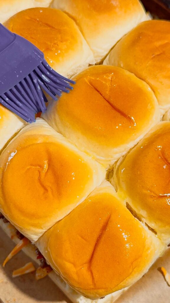 brushing melted butter on top of kings hawaiian rolls