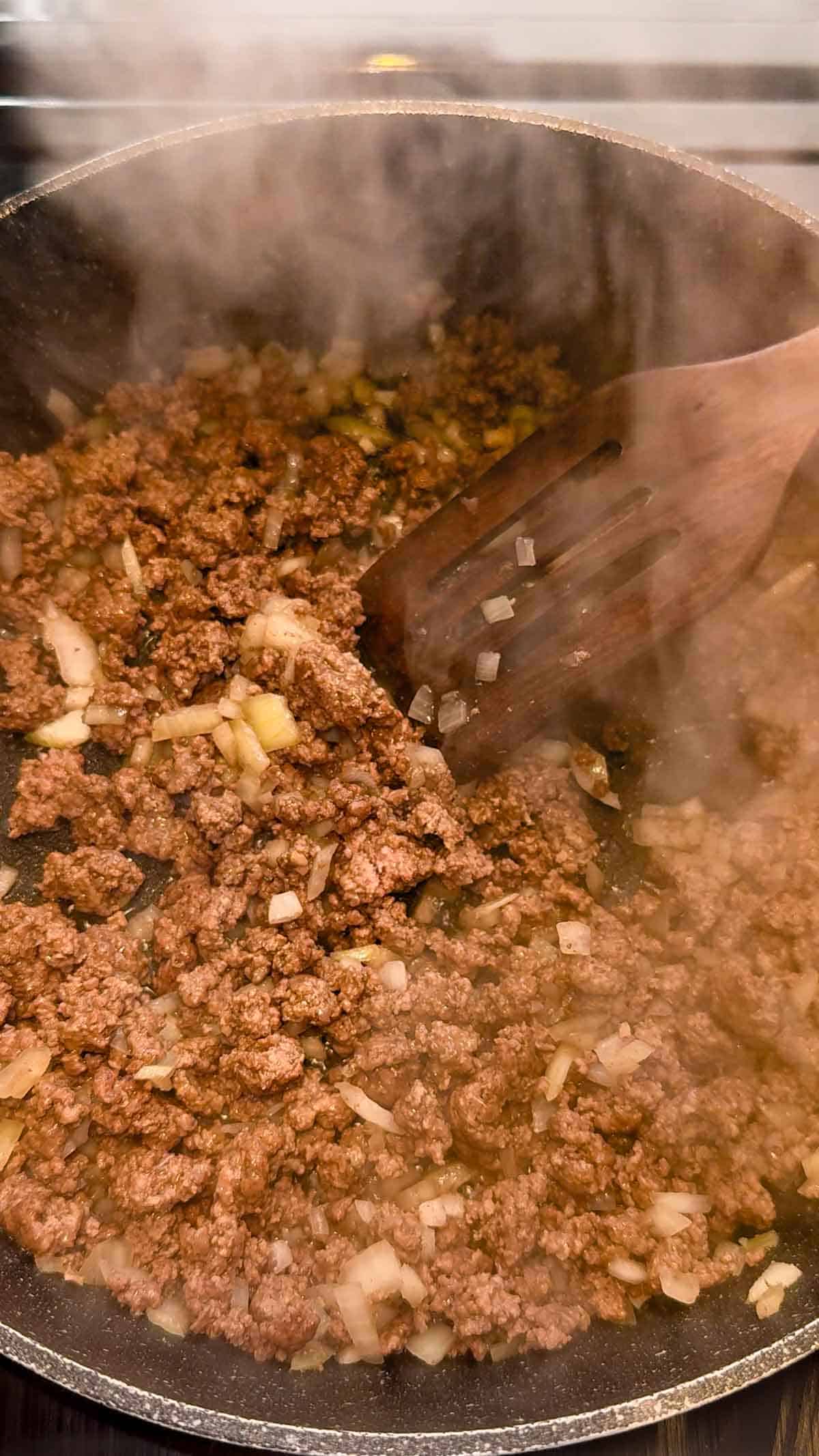 ground beef and diced onions cooking in a skillet