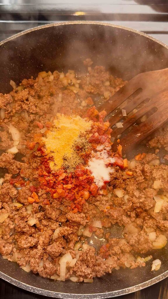 seasonings and crumbled bacon added to skillet with cooked ground beef mixture.