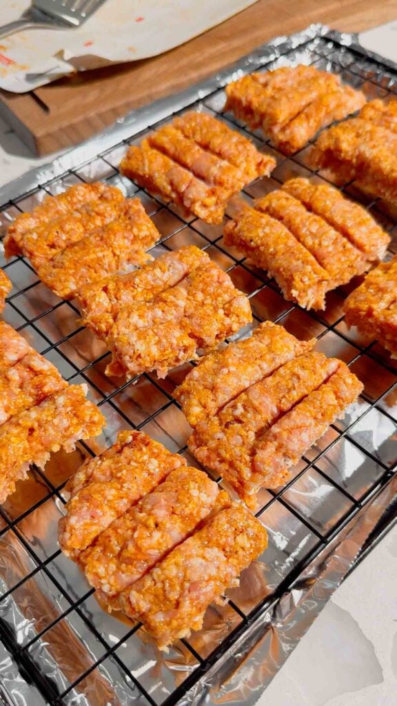 raw mini mcrib patties on a wire rack on a foil lined baking sheet