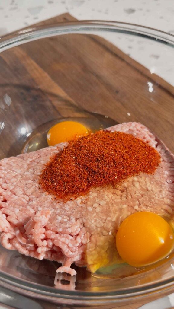 eggs and bbq seasoning added to a bowl with raw ground pork