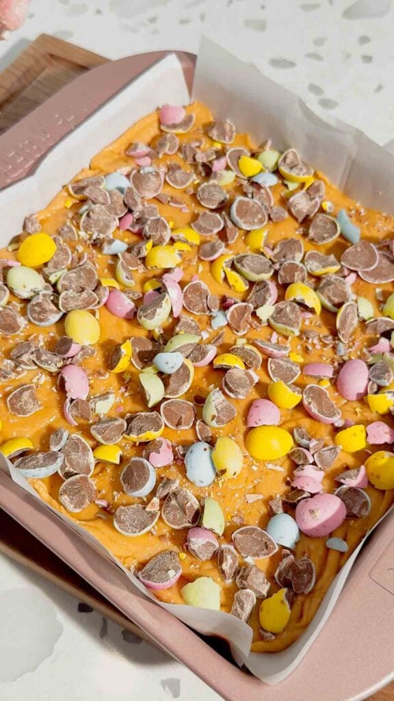 Mini Egg Peanut Butter Cup Fudge is the ultimate easy no bake dessert for Easter and spring parties. This microwave fudge recipe is made with vanilla frosting, peanut butter chips and smooth peanut butter for a rich and creamy texture. Loaded with mini Reese’s peanut butter cups and crushed Cadbury mini eggs, this dessert is perfect for peanut butter lovers. If you’re looking for easy Easter desserts, no bake fudge recipes, simple desserts for a crowd or quick holiday treats, this one is a must try. Great for gifting, dessert trays, potlucks and family gatherings, this sweet treat is colourful, fun and incredibly easy to make. Save this easy fudge recipe for your Easter dessert ideas.