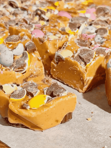 Mini Egg Peanut Butter Cup Fudge is the ultimate easy no bake dessert for Easter and spring parties. This microwave fudge recipe is made with vanilla frosting, peanut butter chips and smooth peanut butter for a rich and creamy texture. Loaded with mini Reese’s peanut butter cups and crushed Cadbury mini eggs, this dessert is perfect for peanut butter lovers. If you’re looking for easy Easter desserts, no bake fudge recipes, simple desserts for a crowd or quick holiday treats, this one is a must try. Great for gifting, dessert trays, potlucks and family gatherings, this sweet treat is colourful, fun and incredibly easy to make. Save this easy fudge recipe for your Easter dessert ideas.