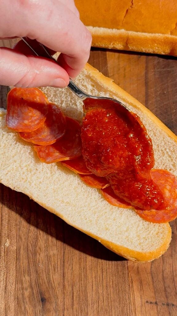 pizza sauce over pepperoni slices on a hot dog bun
