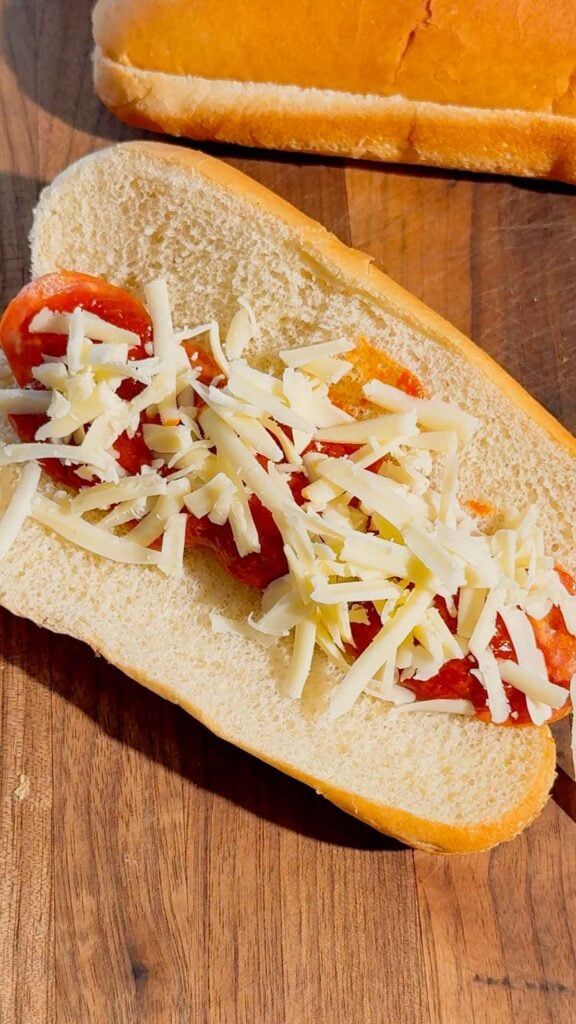 shredded mozzarella, pizza sauce and pepperoni on a hot dog bun