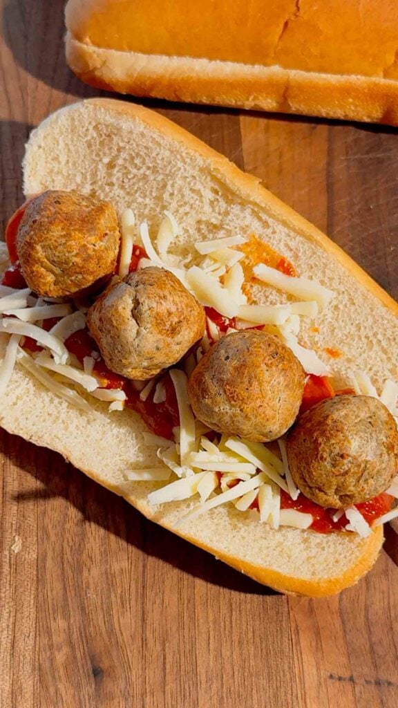 meatballs on top of cheese, pizza sauce and pepperoni on a hot dog bun