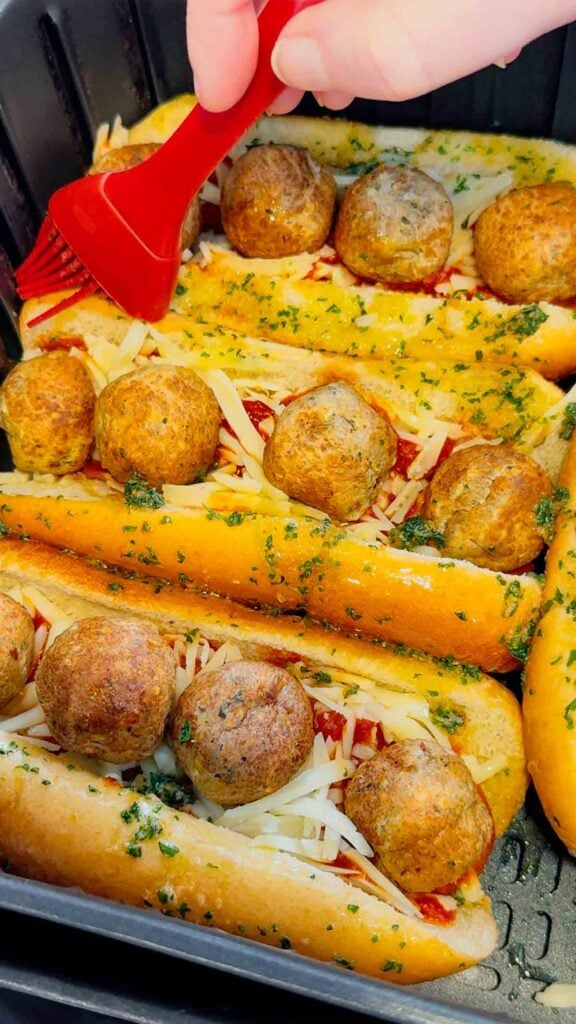 brushing garlic butter on meatball subs