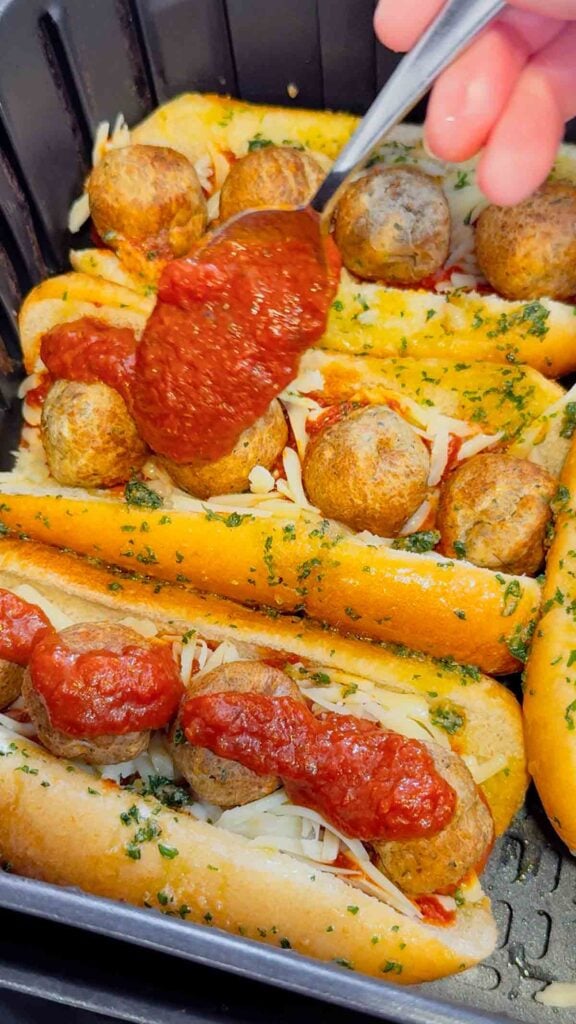 spooning pizza sauce on top of meatball subs