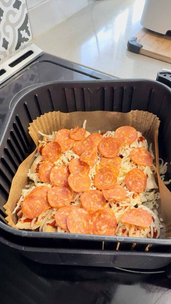 pepperoni slices and shredded mozzarella on top of pierogies in an air fryer basket