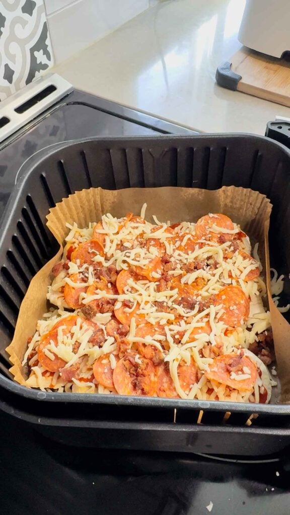 crumbled bacon, pepperoni and cheese on top of pierogies in an air fryer basket