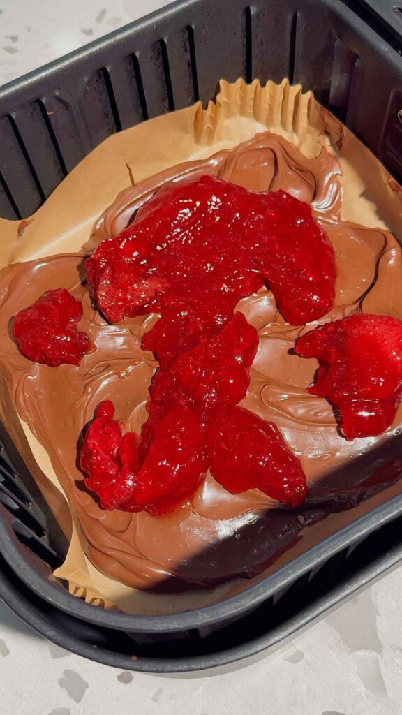 globs of strawberry pie filling spooned over Nutella in an air fryer basket liner