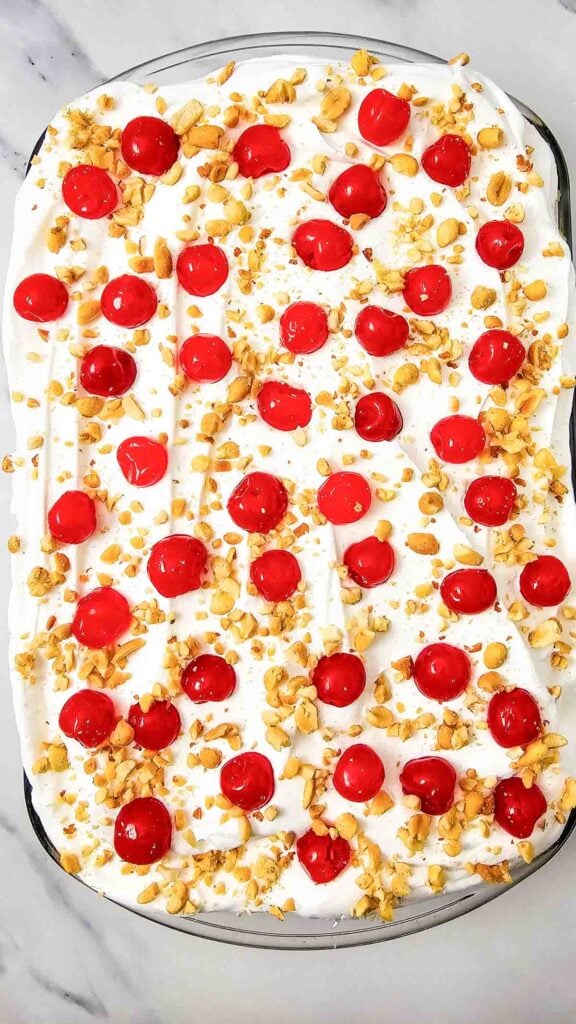 peanuts and cherries on top of whipped topping layer on banana split cake