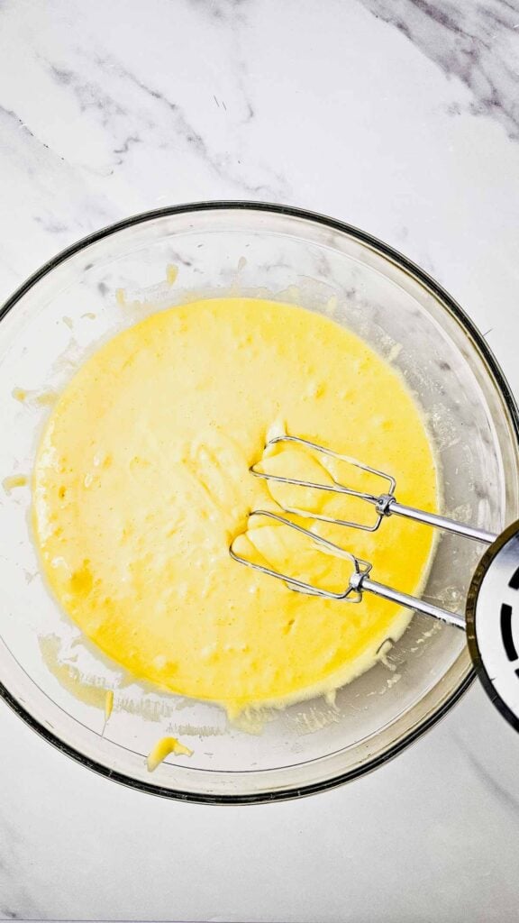 cake batter in a glass bowl with a hand mixer