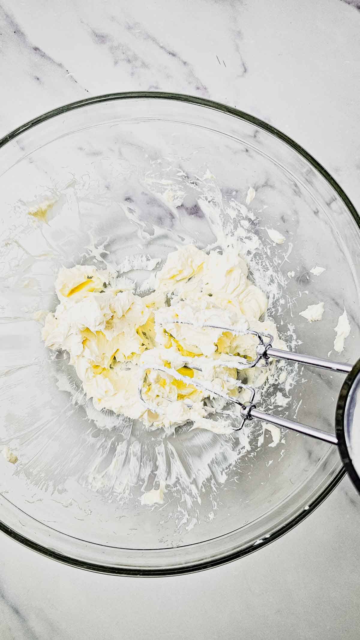 cream cheese being whipped with a hand mixer
