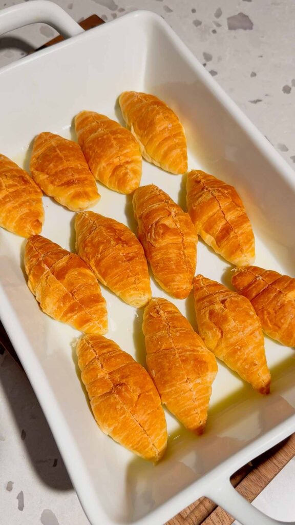 slit mini croissants in a buttered baking dish