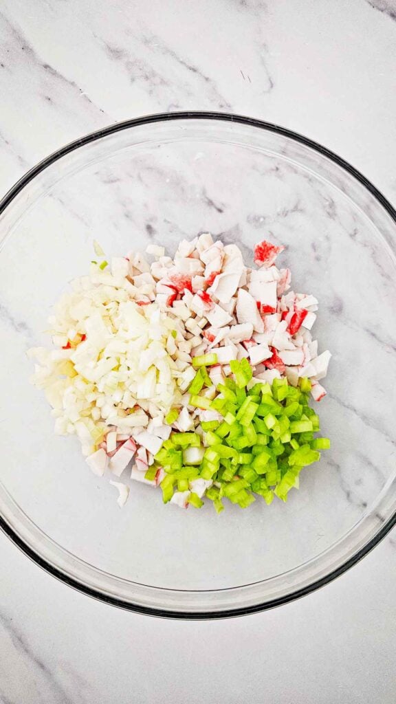 diced onions, diced celery and crab meat in a glass bowl