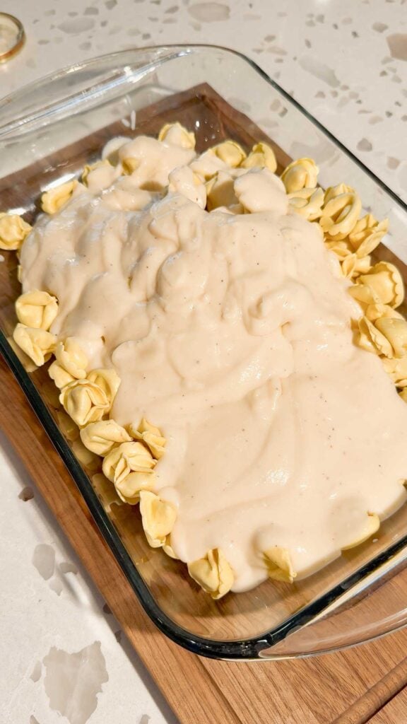 alfredo sauce poured over tortellini in a baking dish