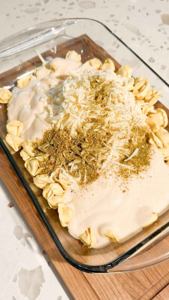 Italian seasoning, shredded mozzarella and alfredo sauce on top of tortellini in a baking dish