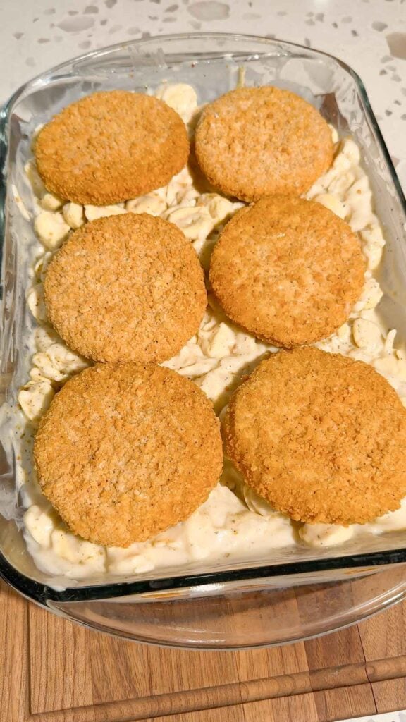 frozen breaded chicken burgers on top of tortellini in alfredo sauce in a baking dish