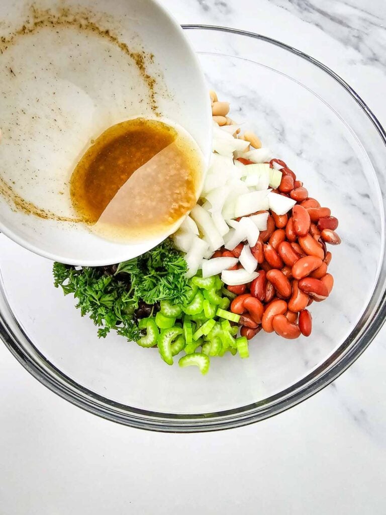 pouring homemade dressing over 3 bean salad ingredientsin a mixing bowl
