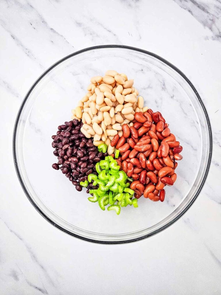 chopped celery, black beans, kidney beans and cannellini beans in a glass mixing bowl