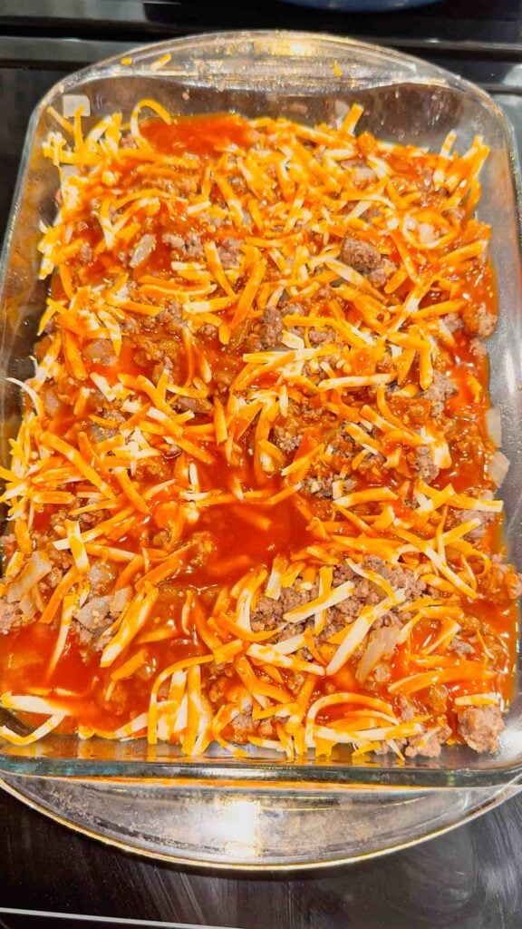 red enchilada sauce and shredded cheddar cheese on top of ground beef and pierogies