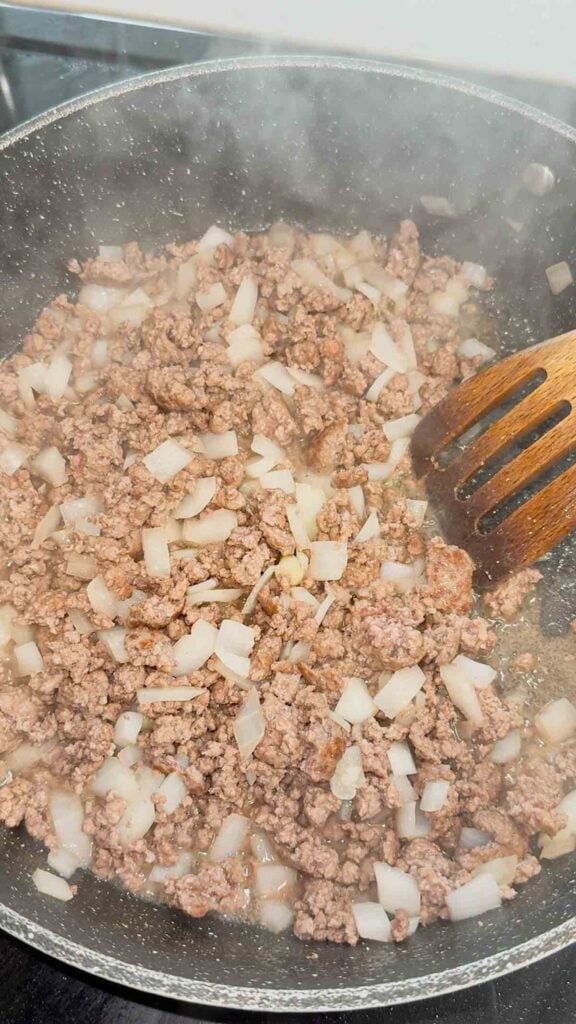 ground beef and diced onions cooking in a skillet