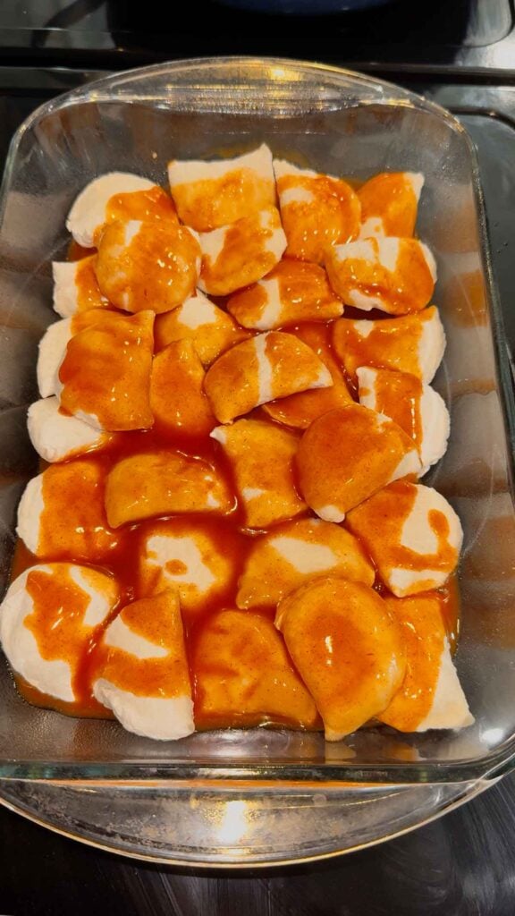 red enchilada sauce on top of frozen pierogies in a baking dish