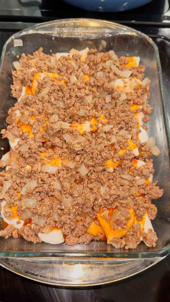 cooked ground beef and red enchilada sauce on top of frozen pierogies in a baking dish