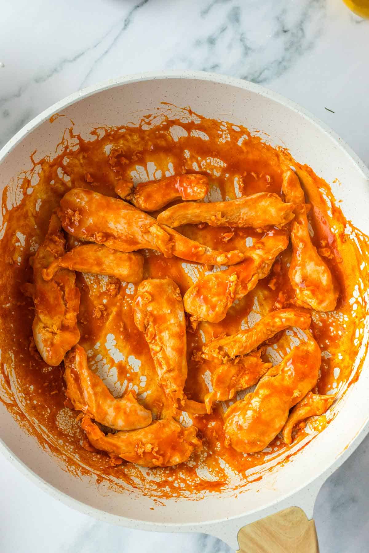 cooked chicken tenders tossed in buffalo sauce in a bowl