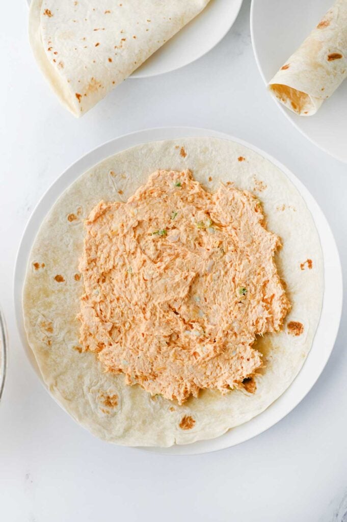 creamy buffalo chicken mixture spread out on a flour tortilla