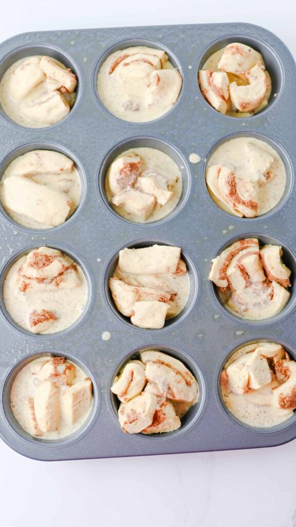 cream and egg mixture poured over cinnamon roll dough chunks in muffin tins