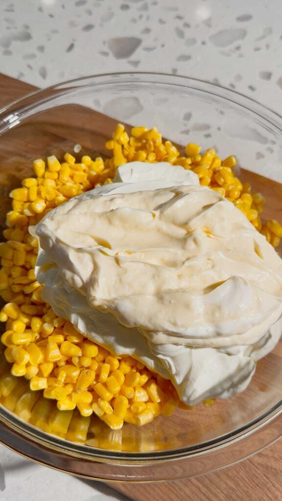mayo and sour cream on top of corn in a mixing bowl