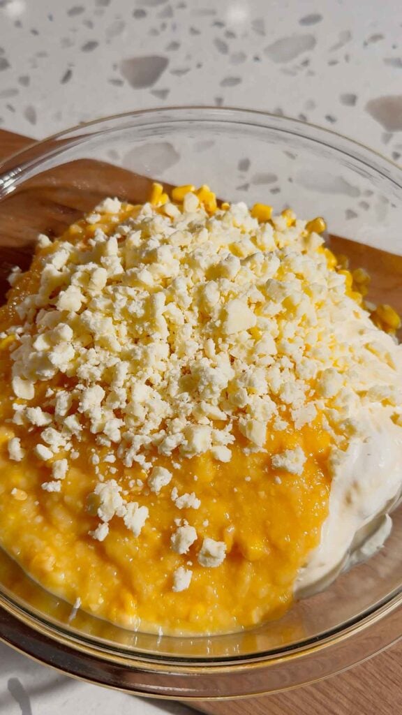 crumbled cotija cheese, cream corn, mayo and sour cream in a mixing bowl