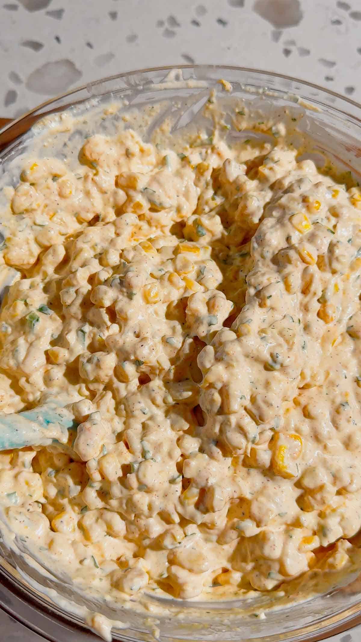 stirring street corn dip in a glass mixing bowl