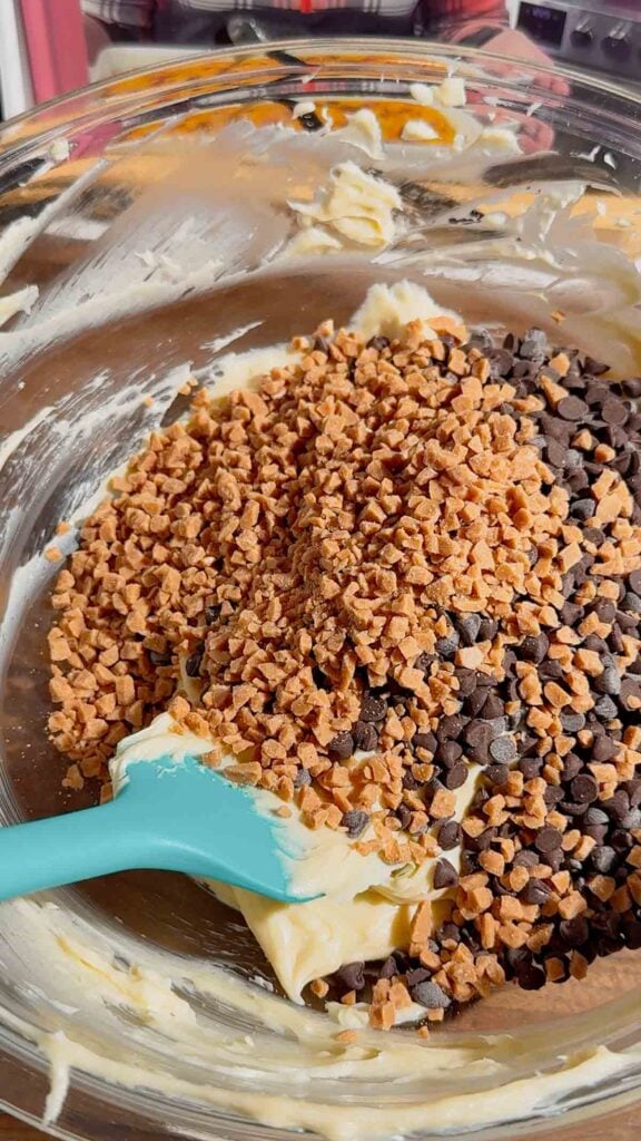 toffee bits and mini chocolate chips on top of cream cheese mixture in a mixing bowl