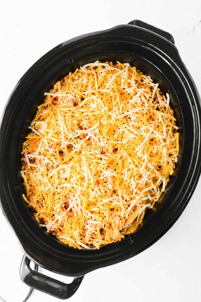 shredded cheese on top of chicken enchilada ingredients in a crockpot
