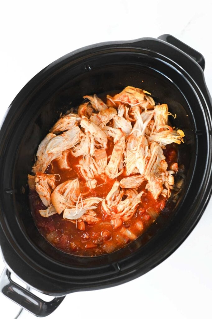 shredded chicken added to crock pot with rotel and enchilada sauce