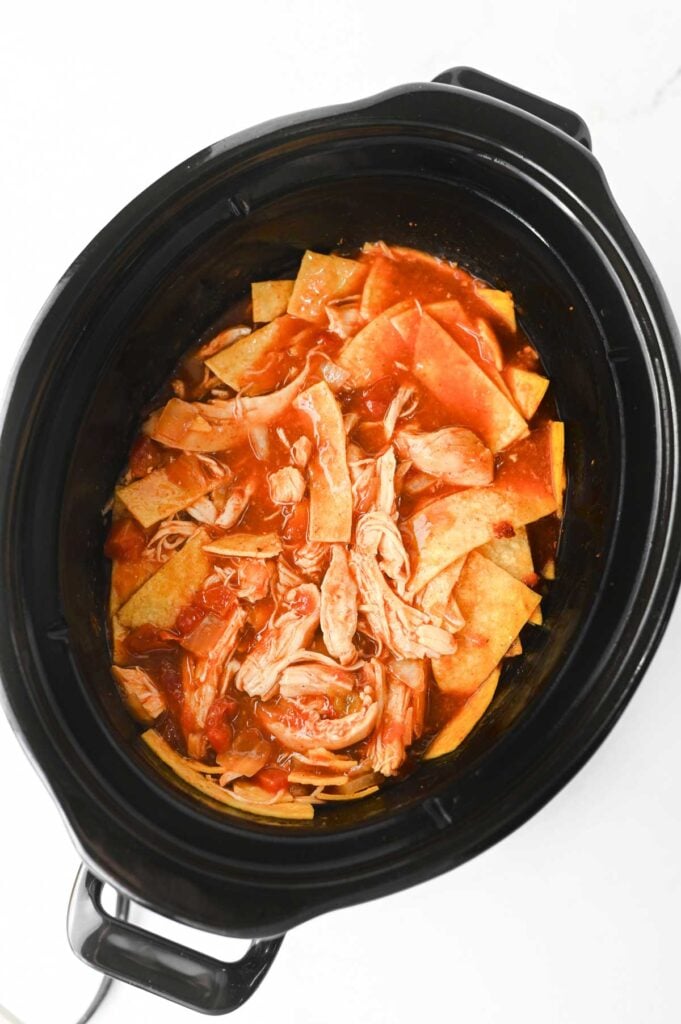 shredded chicken and corn tortillas stirred into slow cooker with enchilada sauce and rotel